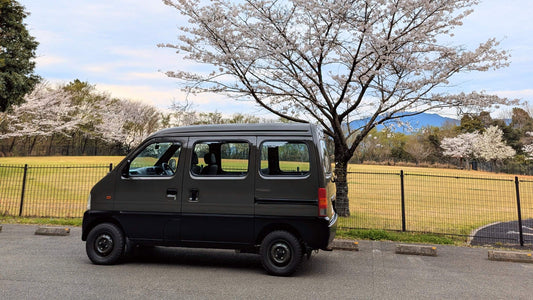 A Green Suzuki Every Van in front of a Japanese Cherry Tree